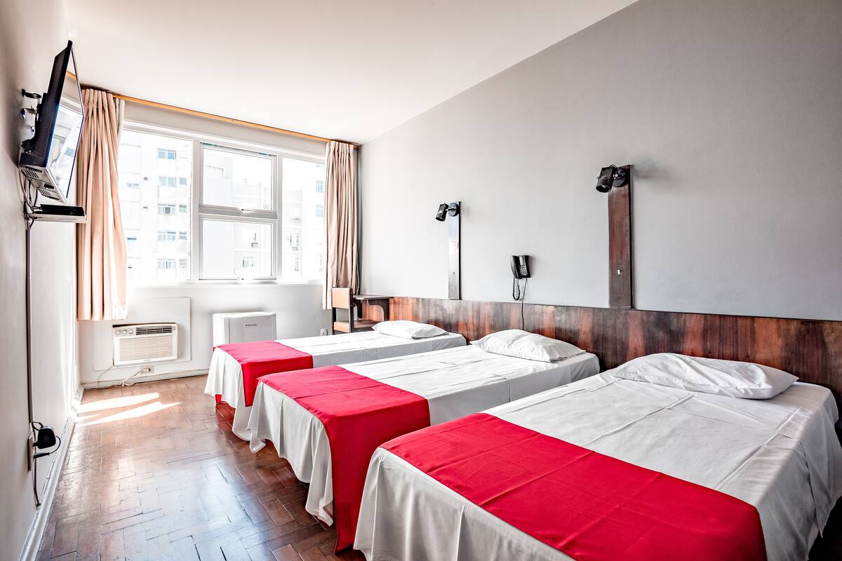 A hotel room with two beds, a TV, a desk, and a window with curtains.