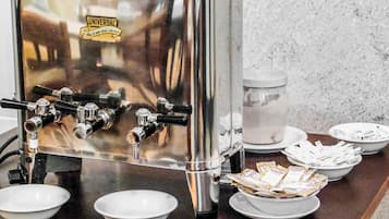 Una máquina de café con varios dispensadores, un recipiente de vidrio y cuencos con servilletas y sobres sobre una encimera.