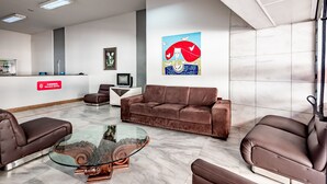 Un moderno vestíbulo de hotel con un mostrador de recepción, asientos cómodos, una mesa de centro de vidrio y un gran cuadro abstracto en la pared.