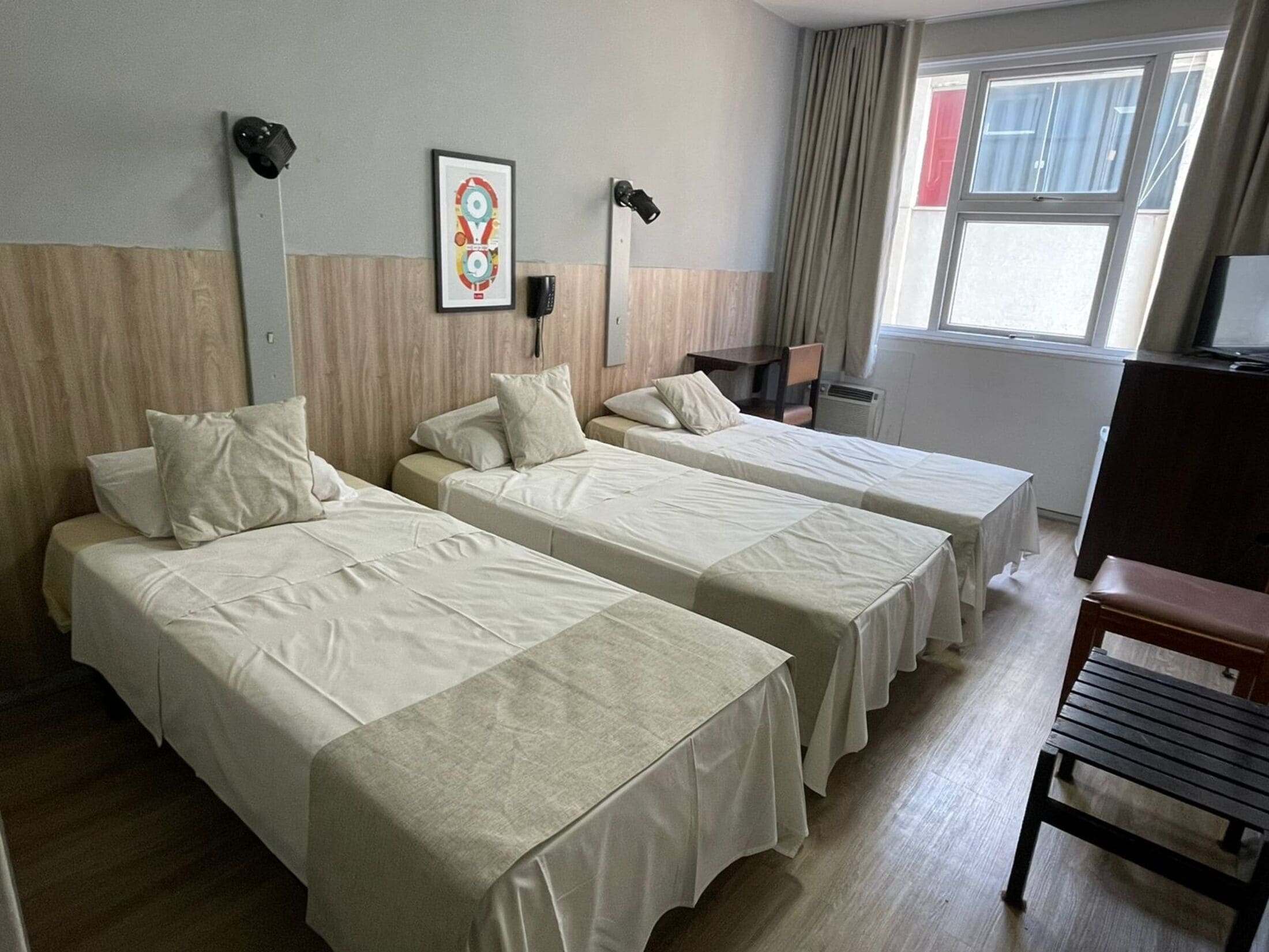 A hotel room with two single beds, a desk, a chair, a TV, and a window with curtains.