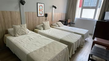 A hotel room with two single beds, a desk, a chair, a TV, and a window with curtains.
