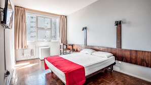 Habitación de hotel con cama, escritorio, silla, televisor y ventana con cortinas.