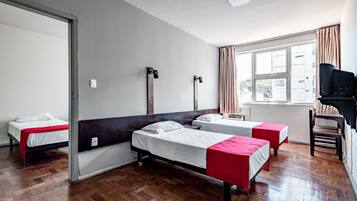 Quarto de hotel com duas camas de solteiro, uma escrivaninha com cadeira, televisão e janela com cortinas.