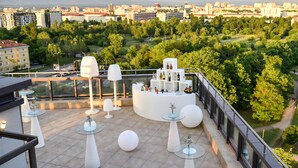 A rooftop terrace with a bar area, round tables, and a view of a cityscape. - Suite Hotel Sofia (Sofia)