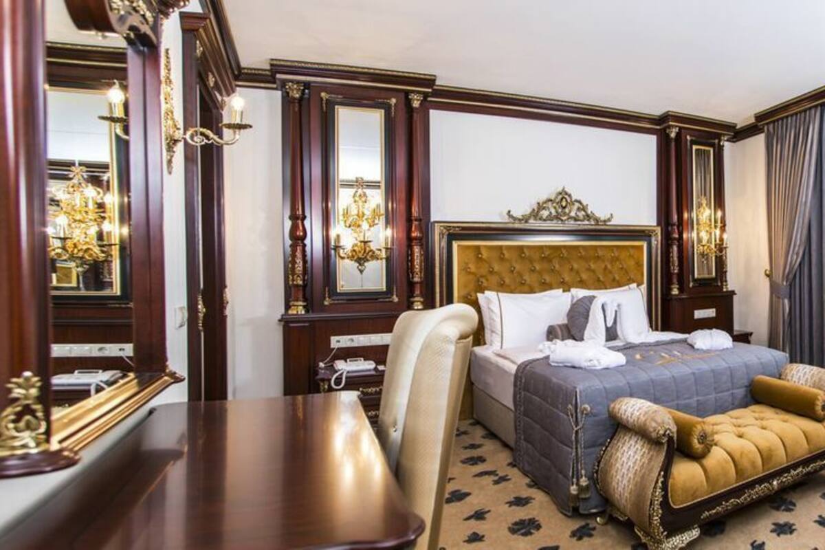 Habitación de hotel con una cama grande, un escritorio y una silla. Hay dos mesitas de noche con lámparas y un espejo.