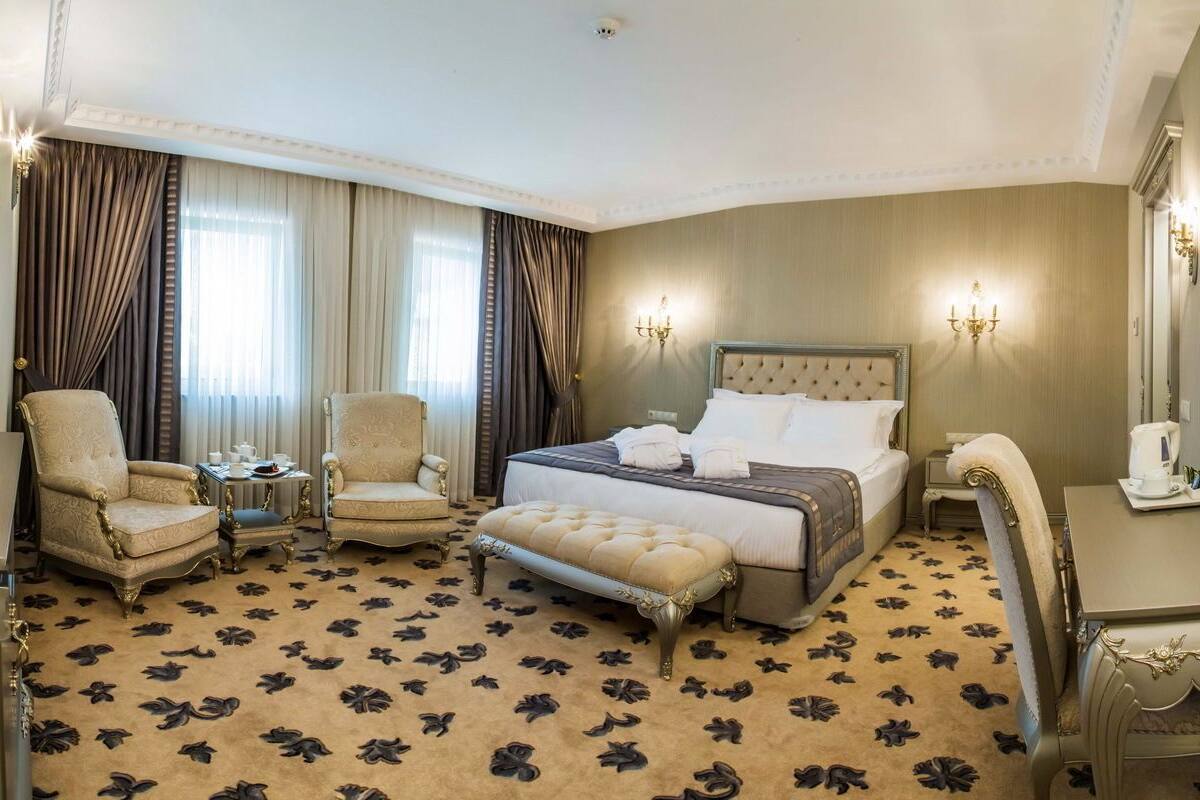 Habitación de hotel con una cama grande, dos sillones, una mesita, un banco, un televisor y un espejo.