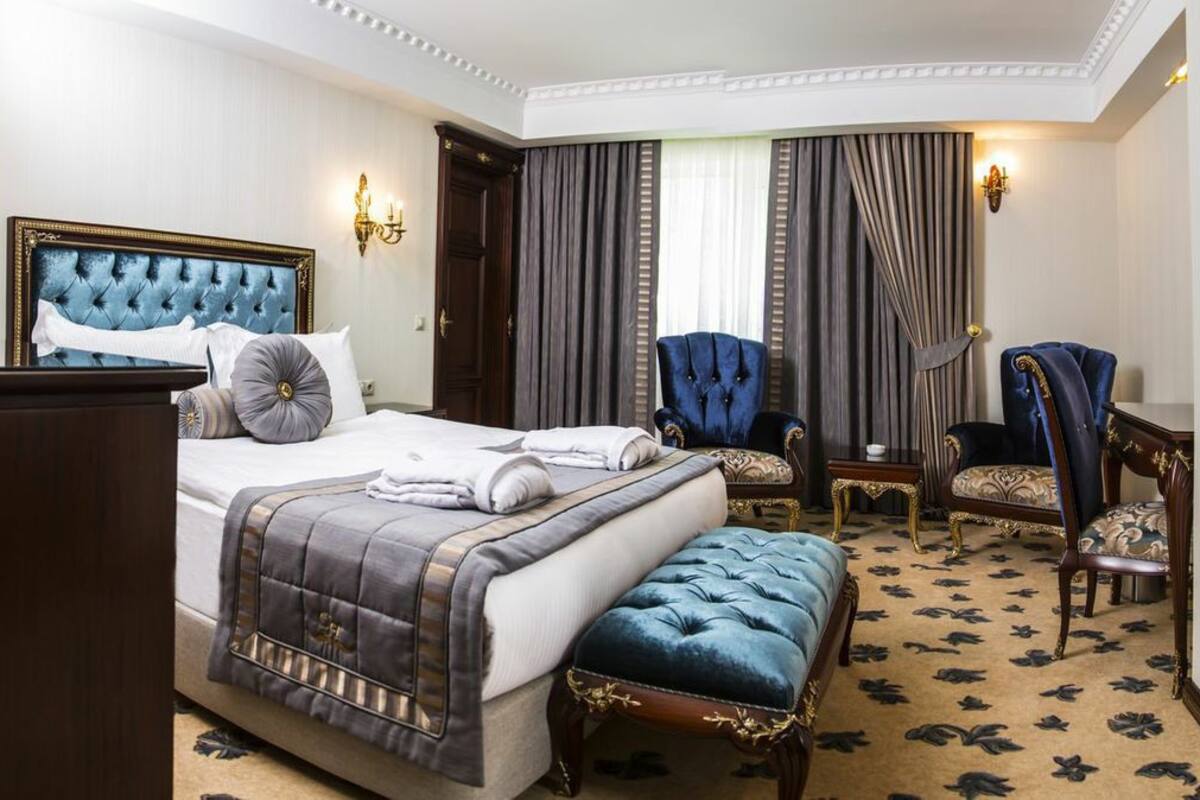 Habitación de hotel con una cama grande, dos sillones, una mesita y un cabecero decorativo.