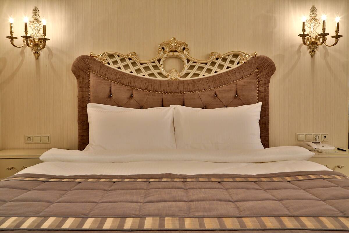 Una cama grande con cabecera capitonada, dos apliques de pared y una mesita de noche con un teléfono y un bloc de notas.