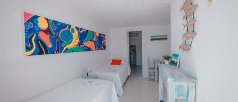 A room with two single beds, a desk, a colorful abstract painting, and a wall-mounted fish decoration.