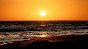 Una puesta de sol sobre el océano, con una playa en primer plano.