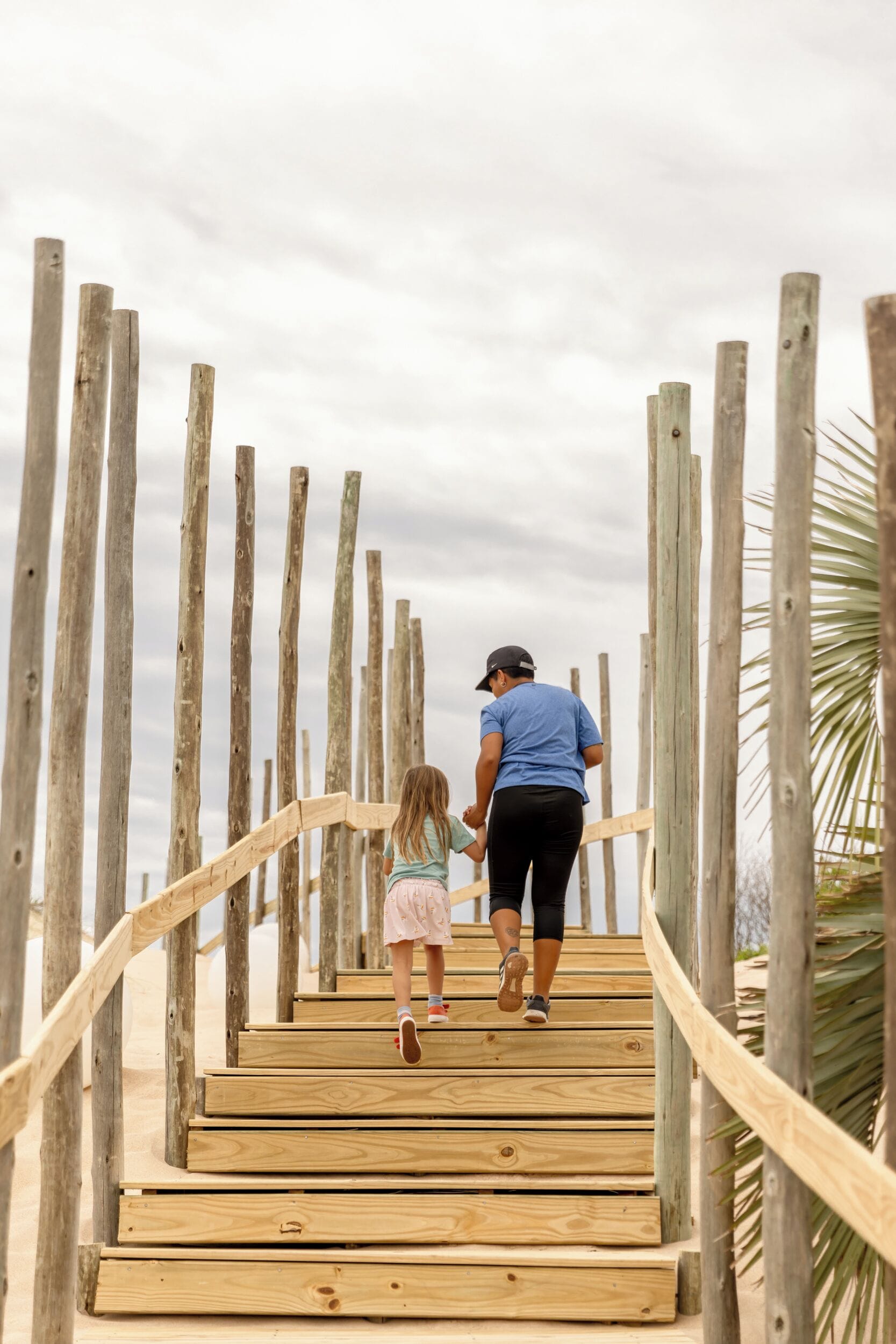 En trätrappa leder ner till ett område vid stranden, och till höger står en palm.