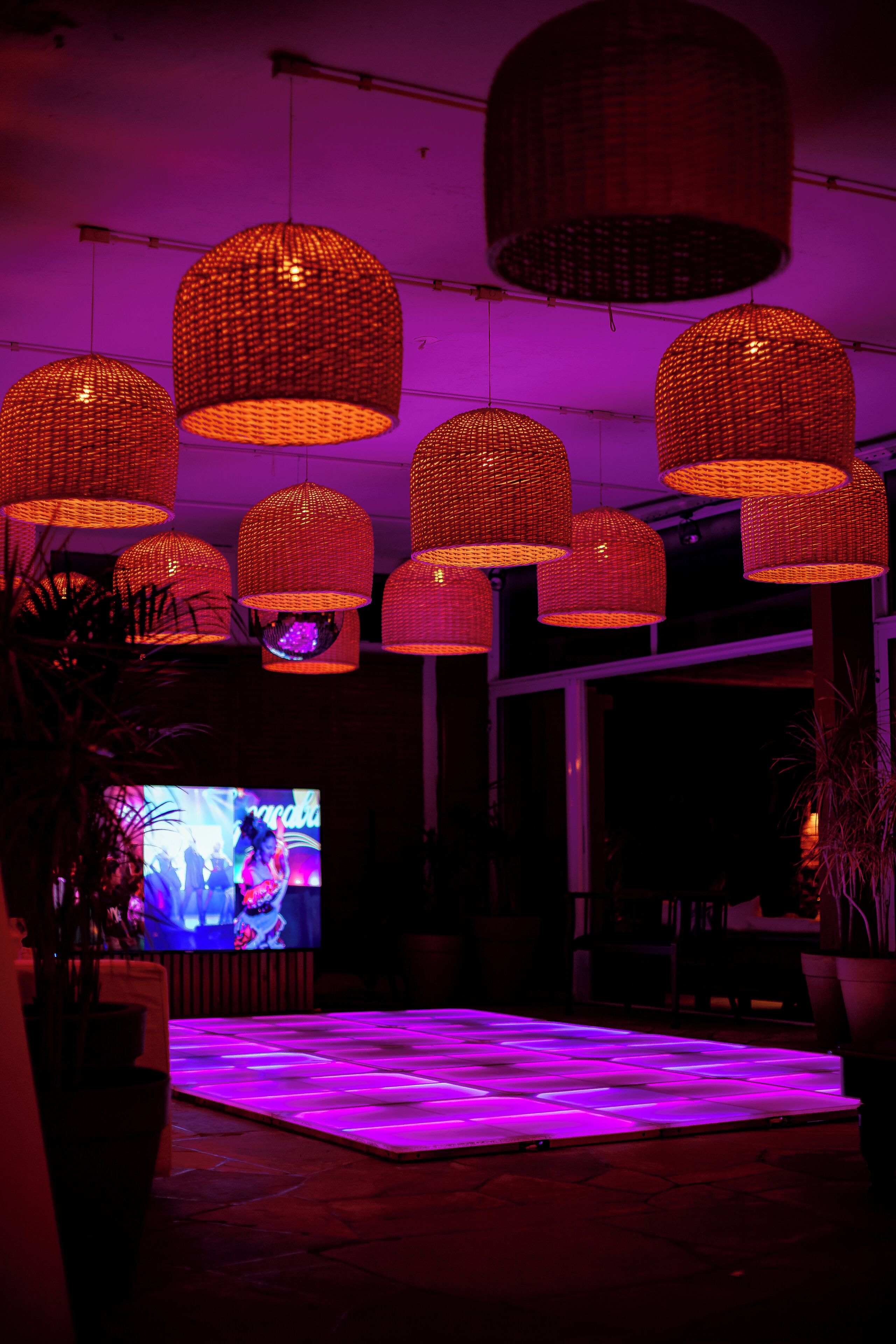 A room with hanging wicker lamps, a flat-screen TV, and a tiled floor.