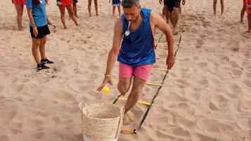 Escena de playa con gente, sombrillas y un hombre caminando sobre una cuerda.