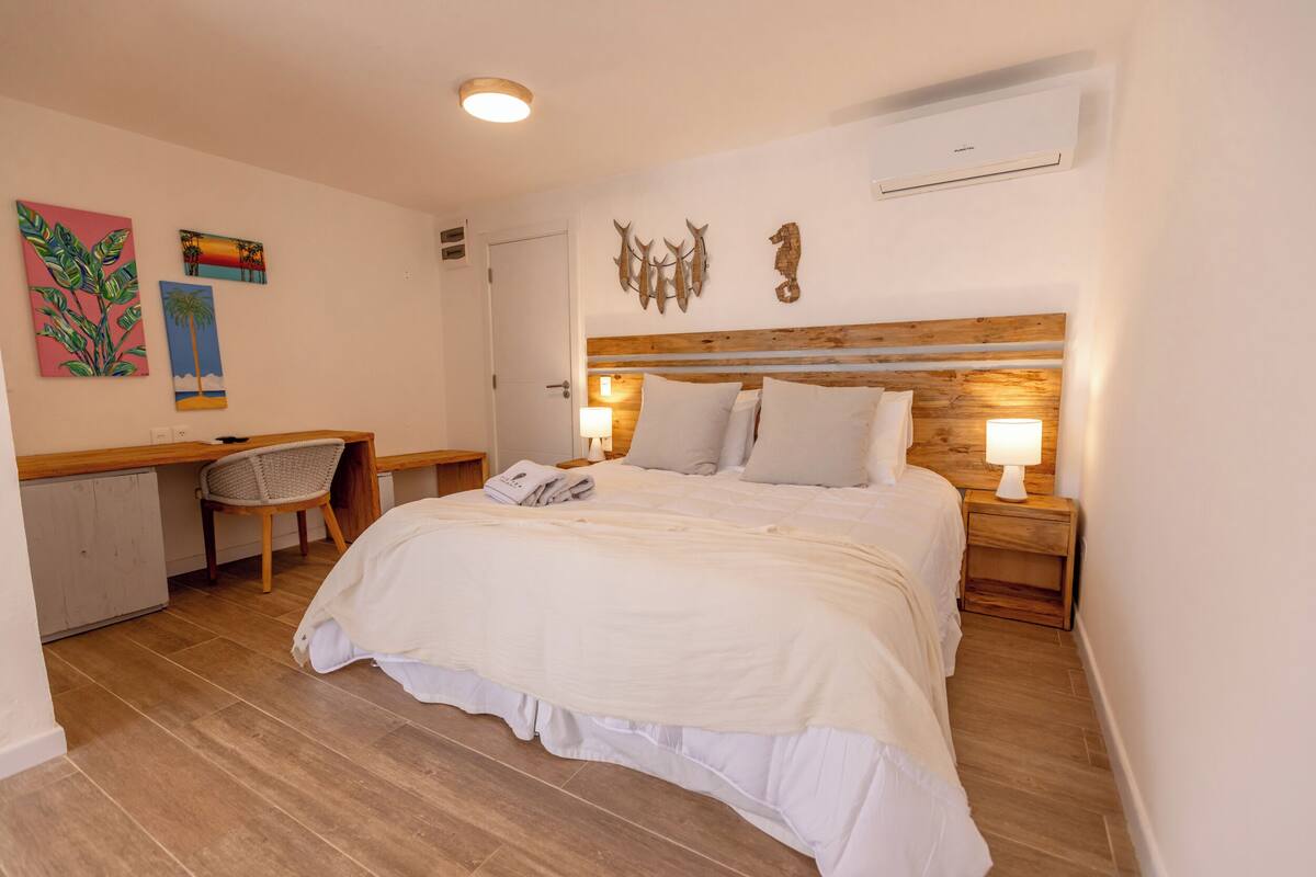 A bedroom with a wooden headboard, a bed with white bedding, a desk with a chair, and wall art.