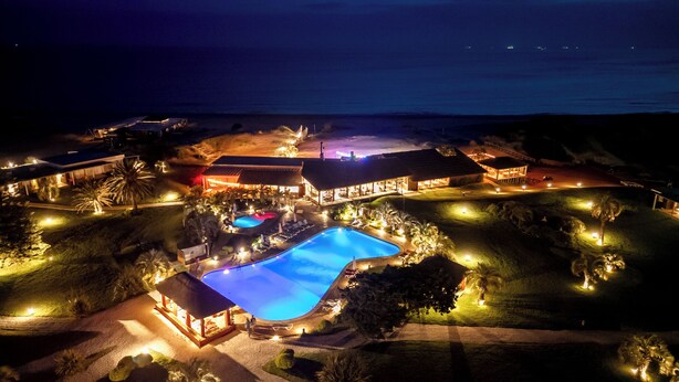 Vista aérea de un resort con piscina, varias edificaciones y una playa.