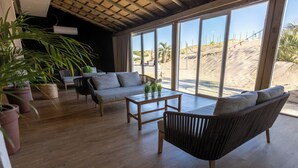Un espacio habitable amplio con sofá, mesa de centro y plantas en macetas. Amplias ventanas ofrecen vistas a la playa.