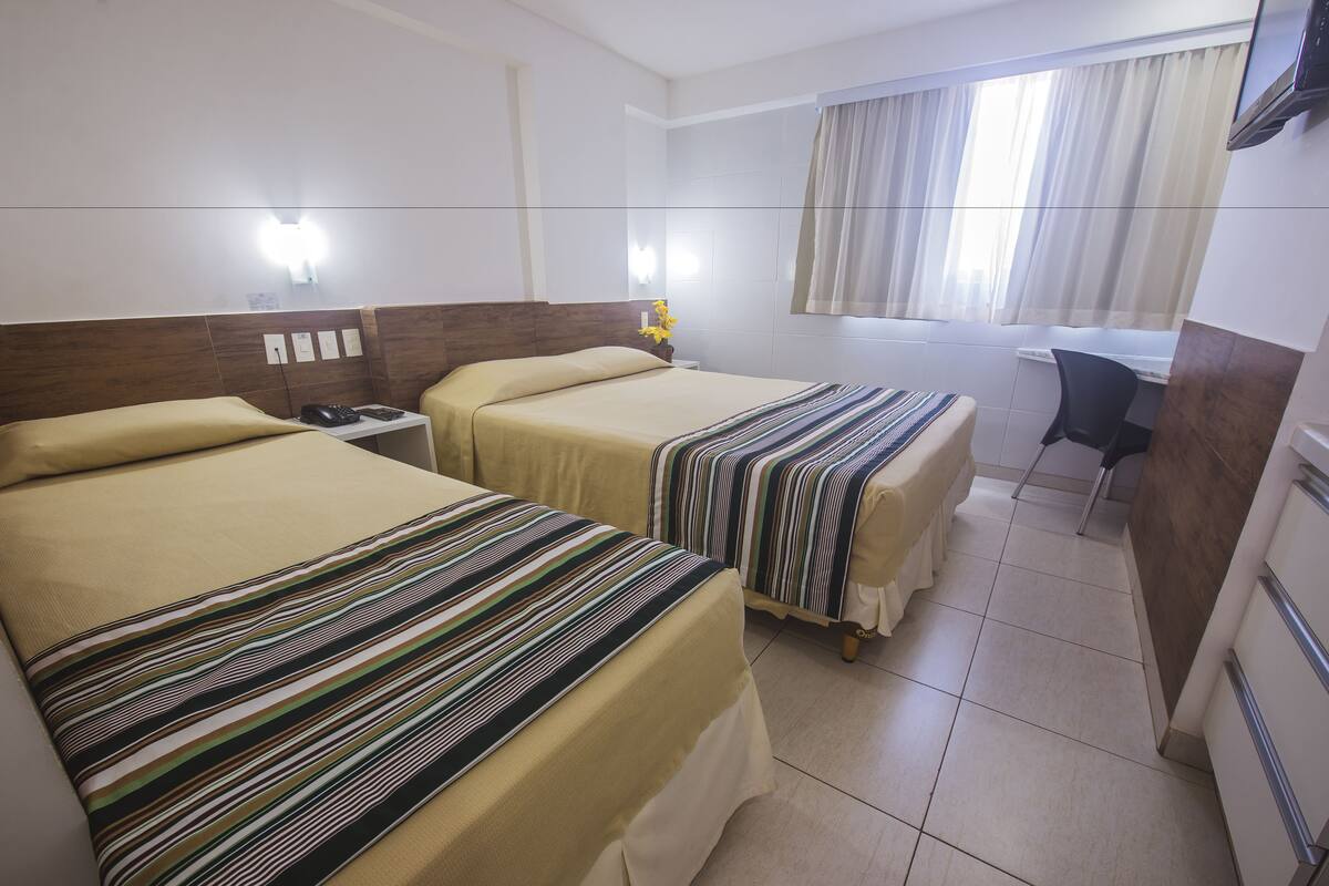 A hotel room with two beds, a desk, and a chair.
