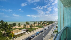 A coastal cityscape with a beach, palm trees, and a modern building with a glass facade.