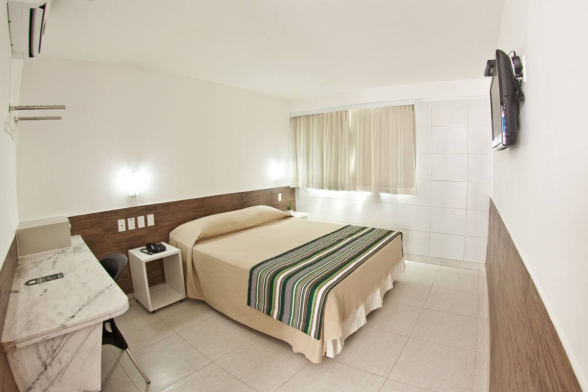 A hotel room with a bed, bedside table, and a desk with a chair.