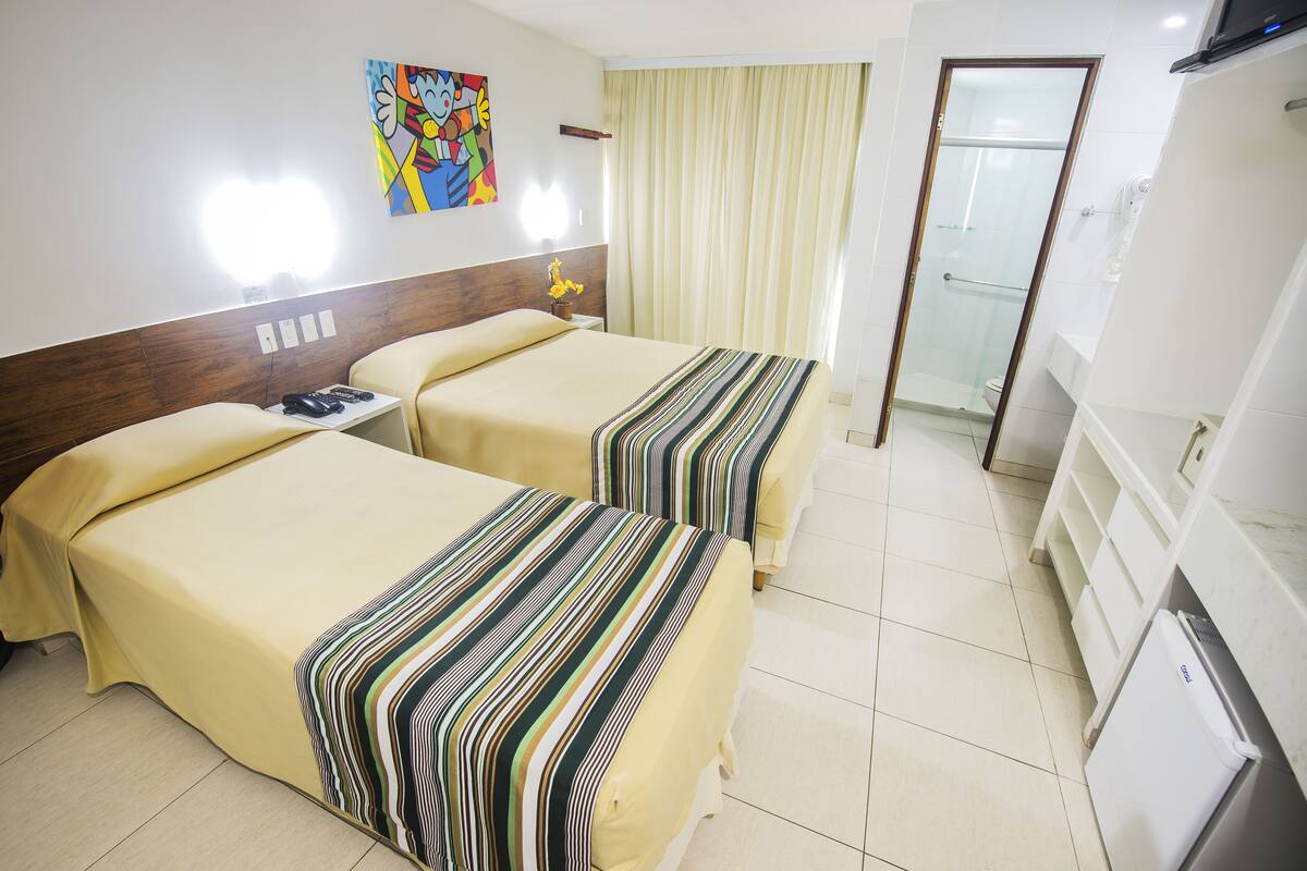 A hotel room with two beds, a shower, a small refrigerator, and a television.