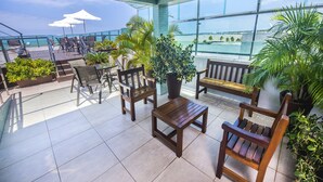 A terrace with wooden furniture, potted plants, and a view of the sea.