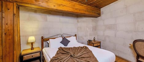 A wooden-framed bedroom with a bed, a nightstand, a lamp, and a chair.