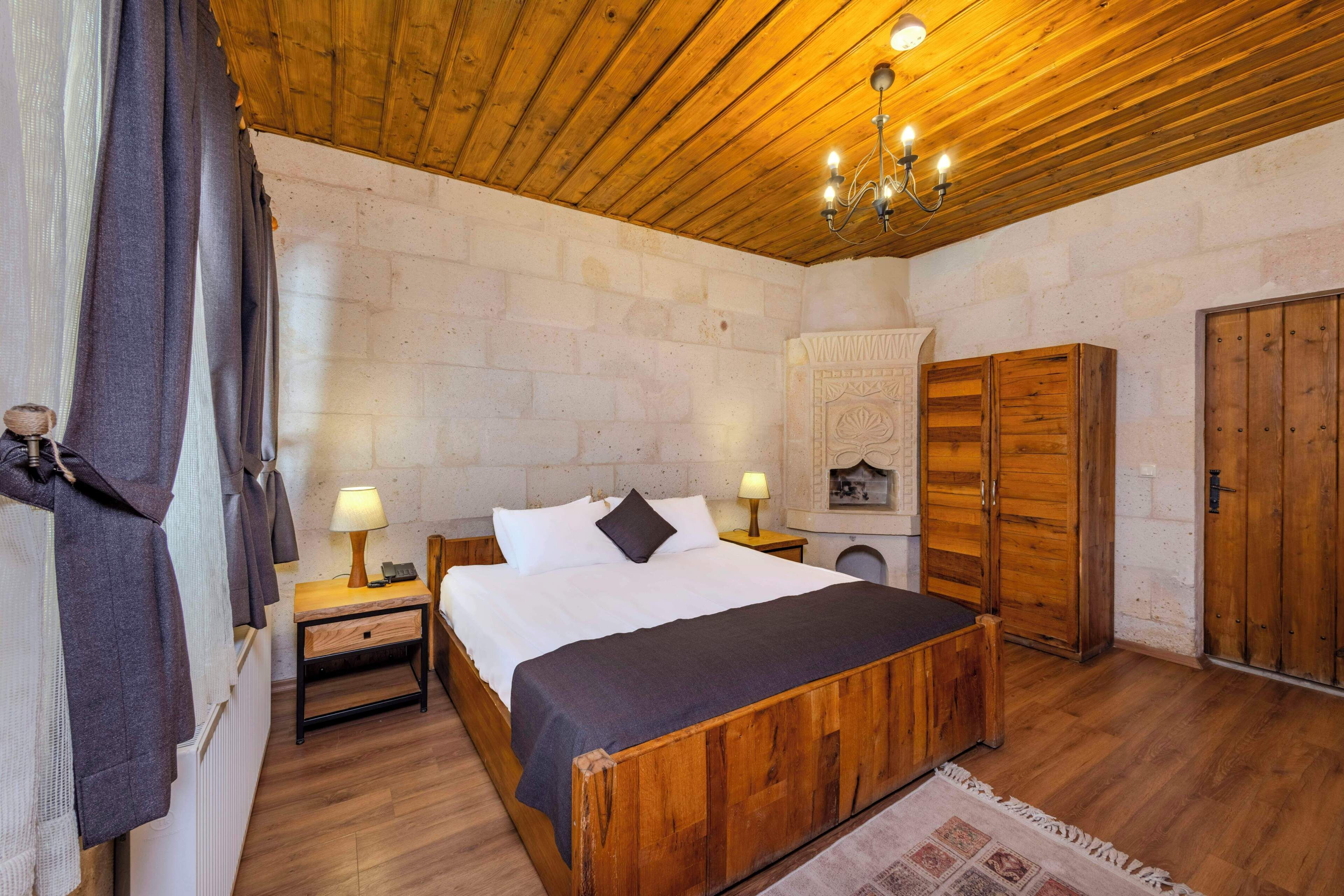 A bedroom with a wooden bed, two bedside lamps, a wardrobe, and a stone wall.