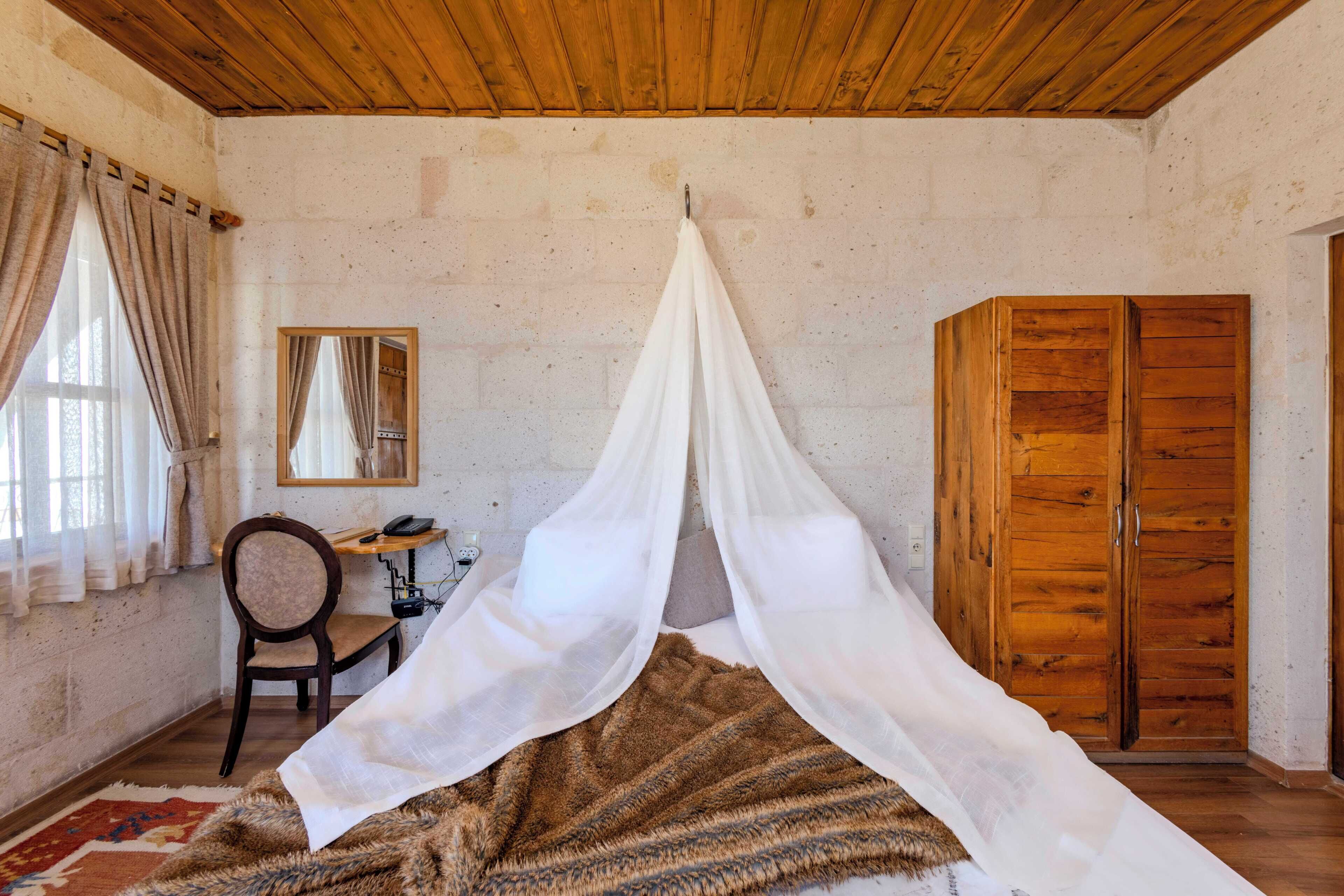 Une chambre à coucher avec un lit à baldaquin, une armoire en bois, un bureau avec une chaise et un miroir au mur.