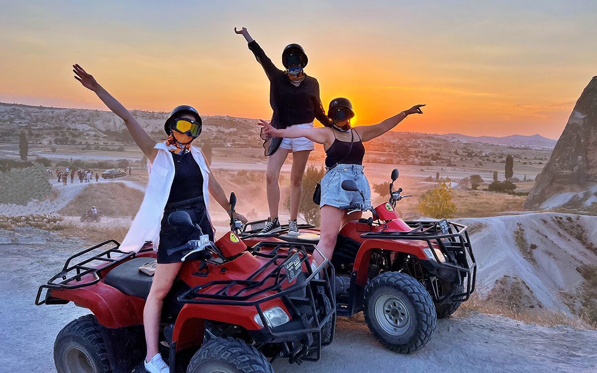 Three people on ATVs with their arms raised against a sunset backdrop.