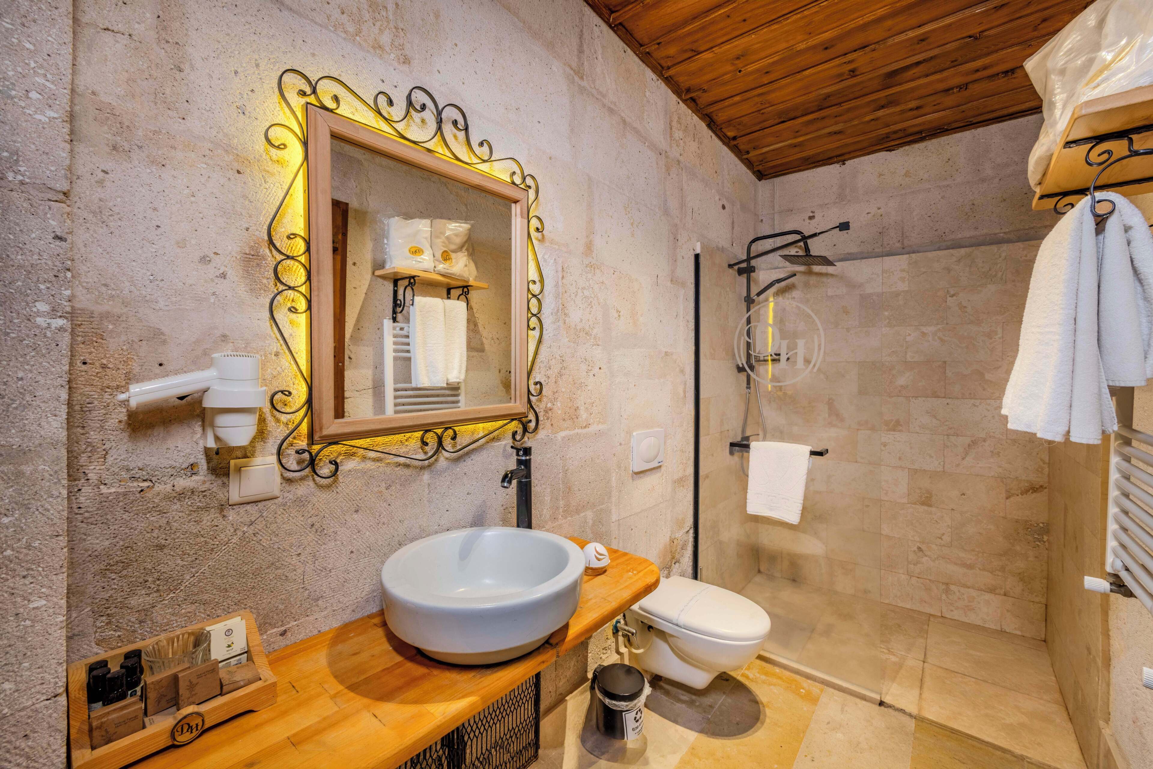 A bathroom with a wooden vanity, a white sink, a toilet, a shower area, and a mirror with a decorative frame.