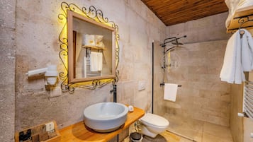 Ein Badezimmer mit einem Holzbidet, einem weißen Waschbecken, einer Toilette, einer Duschkabine und einem Spiegel mit dekorativem Rahmen.