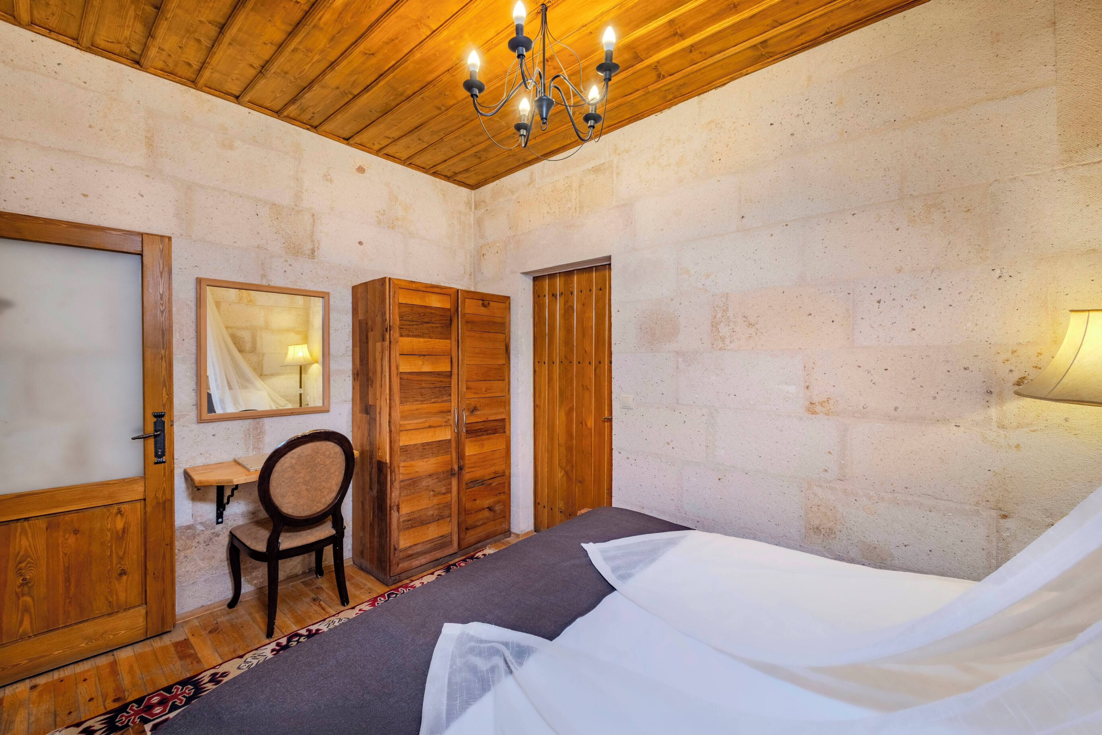 A bedroom with a bed, a chair, a desk, a wardrobe, and a mirror.
