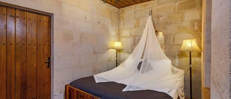 A bedroom with a wooden bed, a canopy, a nightstand with a lamp, and a stone wall.