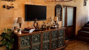 Une pièce dotée d’un plancher en bois, d’une grande armoire en bois ornée de panneaux métalliques décoratifs, d’un téléviseur fixé au mur et d’un luminaire suspendu.