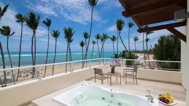 Un balcon doté d’un jacuzzi, de sièges et offrant une vue sur la plage et les palmiers.