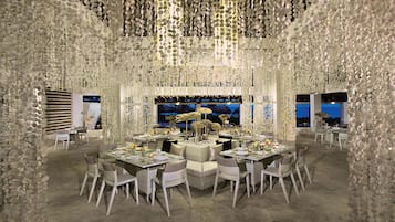 A dining area with round tables, white chairs, and a large aquarium in the background.