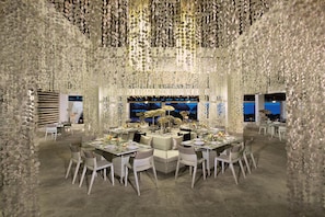 A dining area with round tables, white chairs, and a large aquarium in the background. - Breathless Punta Cana Resort & Spa - Adults Only - All Inclusive (Punta Cana)