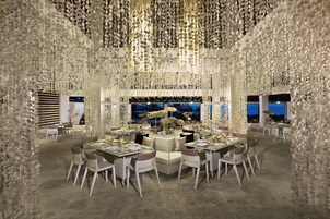 Un comedor con mesas redondas, sillas blancas y un acuario grande al fondo.