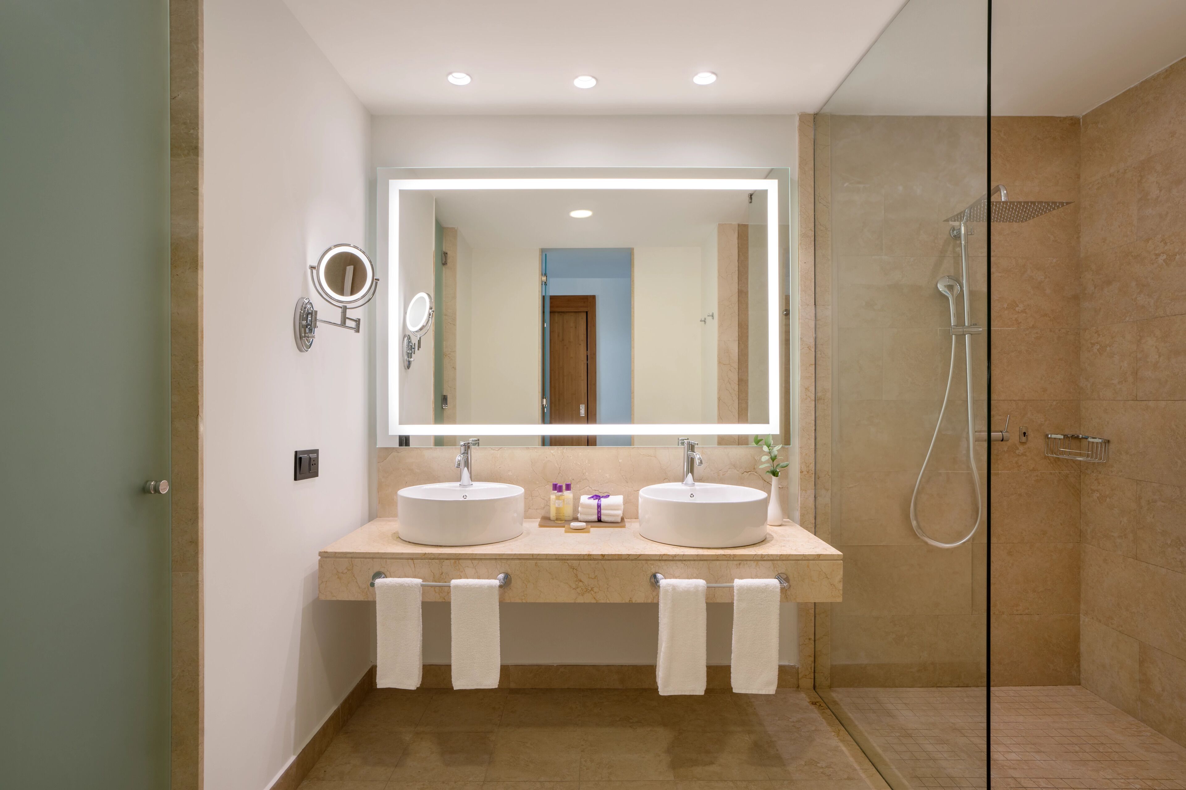A modern bathroom with two sinks, a large mirror, and a glass-enclosed shower.