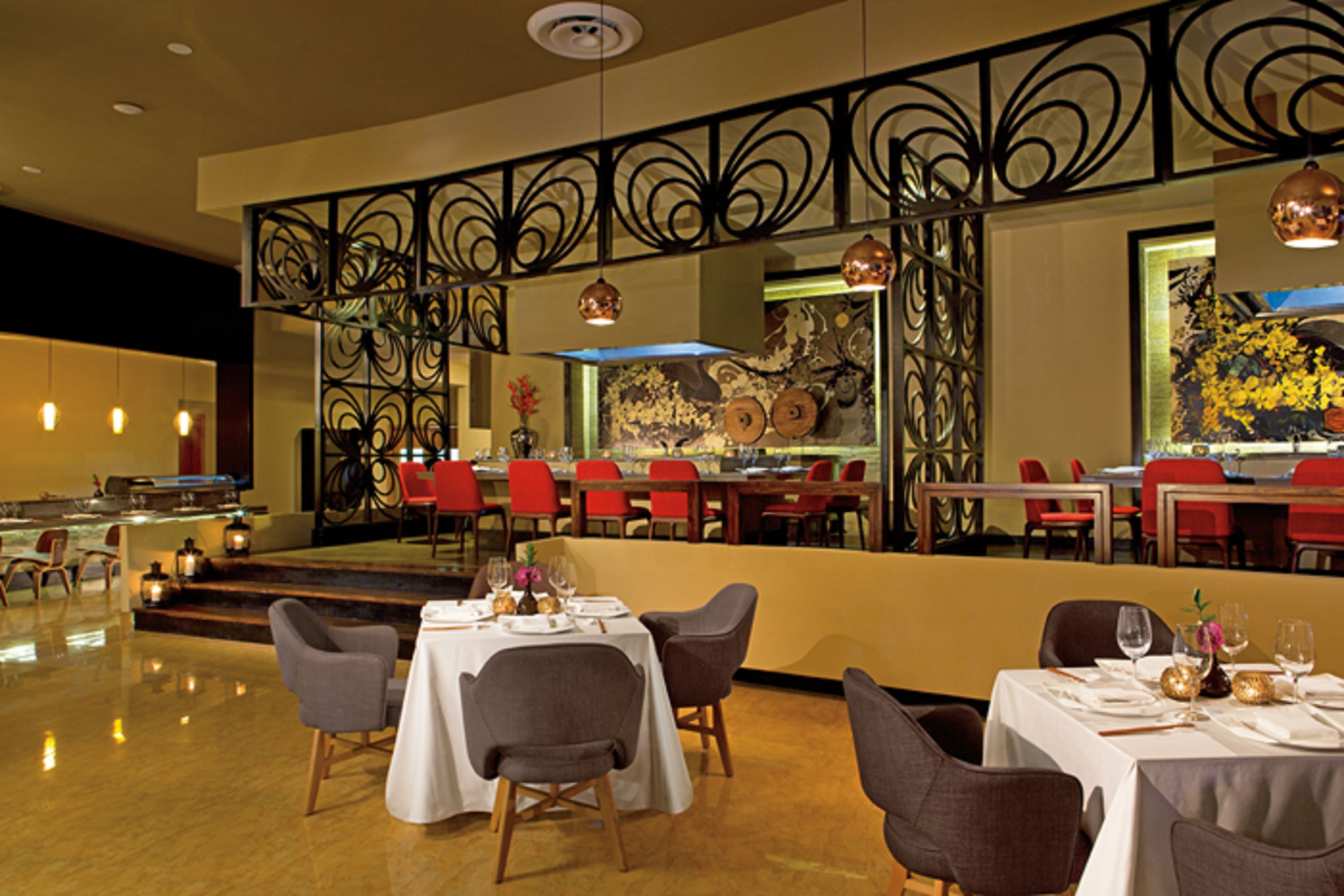 A restaurant with tables set for dining, red chairs, and a decorative metal railing.