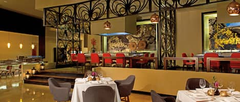 A restaurant with tables set for dining, red chairs, and a decorative metal railing.