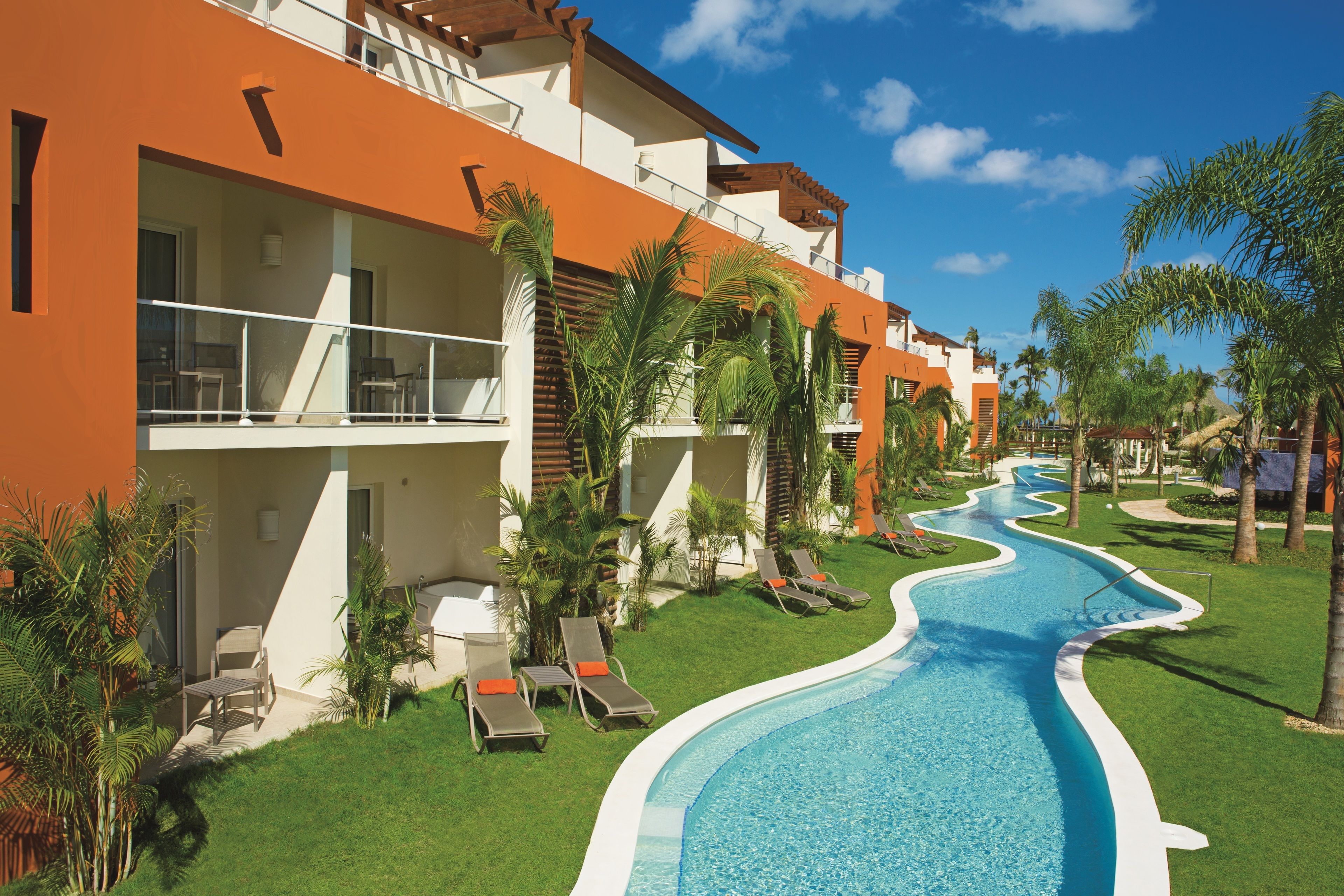 A hotel with a swimming pool, outdoor seating, and palm trees.