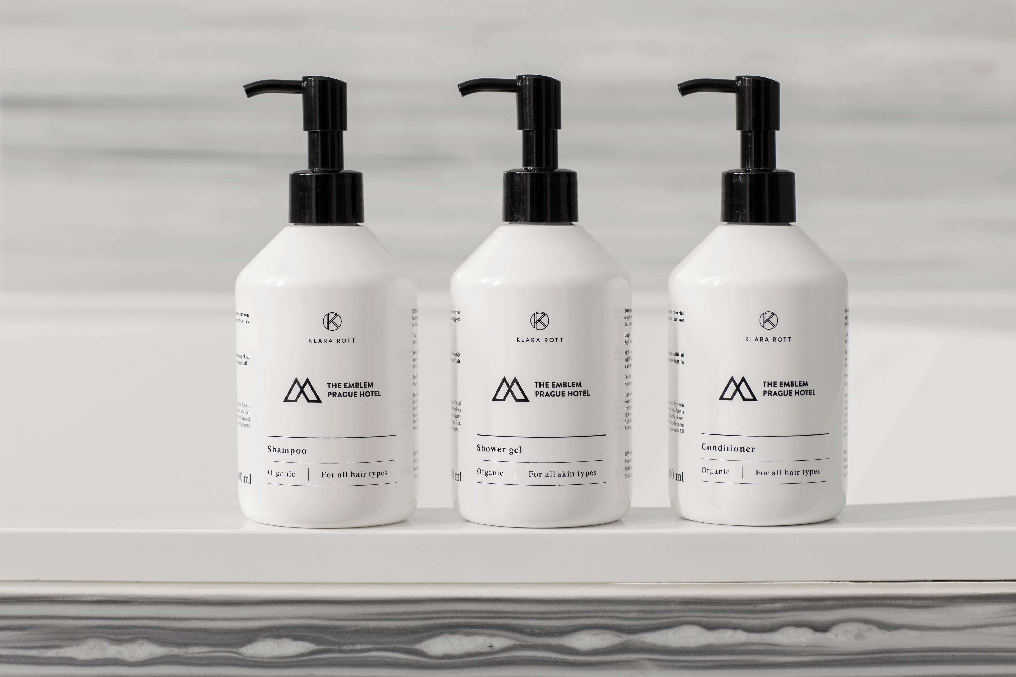 Drie witte flessen van The Emblem Prague Hotel: shampoo, douchegel en conditioner.