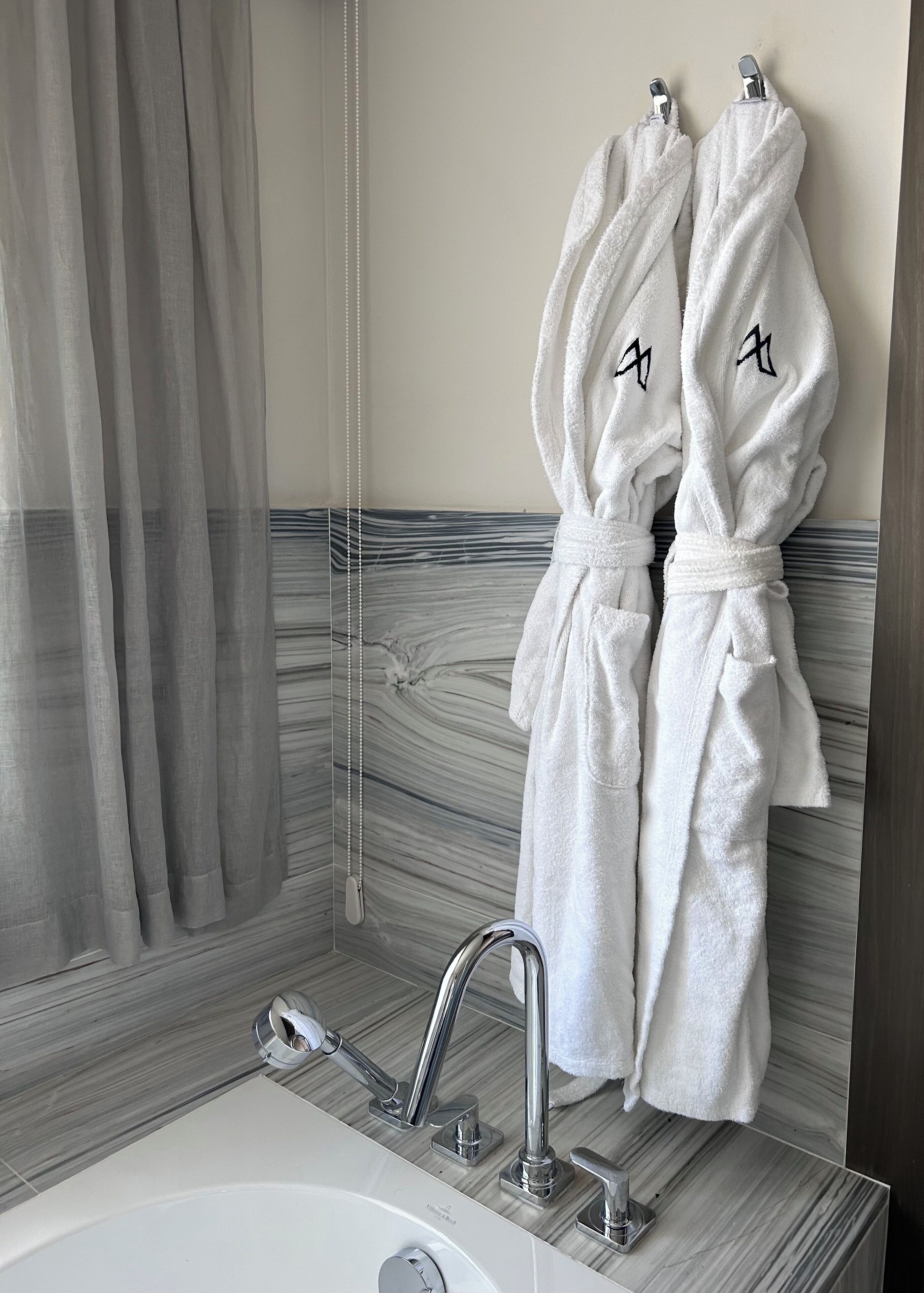 A bathroom with a marble wall, a bathtub, and two white towels hanging on a rack.