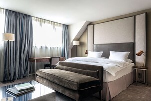 Quarto de hotel moderno com uma cama grande, uma mesa de cabeceira, uma luminária de leitura e um pequeno banquinho.