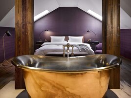 Quarto moderno com uma banheira grande, cama bem arrumada e teto inclinado com claraboias.