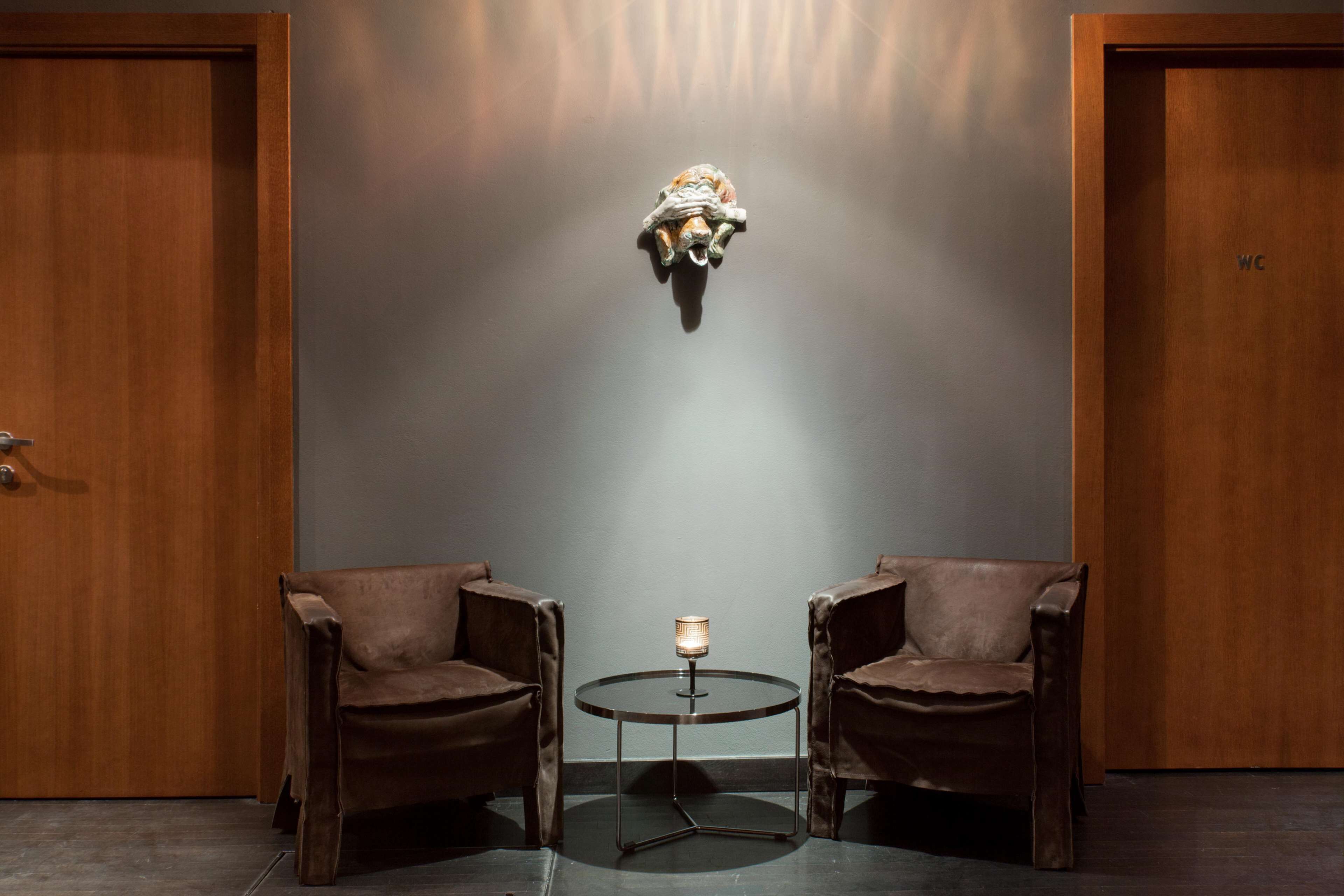 A room with two leather armchairs, a small round table with a lamp, and a wall-mounted light fixture.