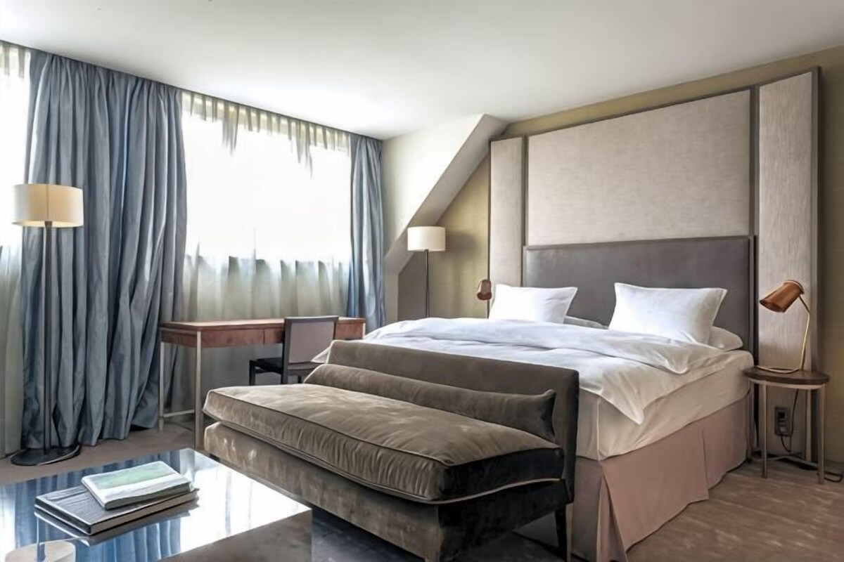 Een hotelkamer met een groot bed, een bureau, een stoel, een klein tafeltje en een raam met gordijnen.