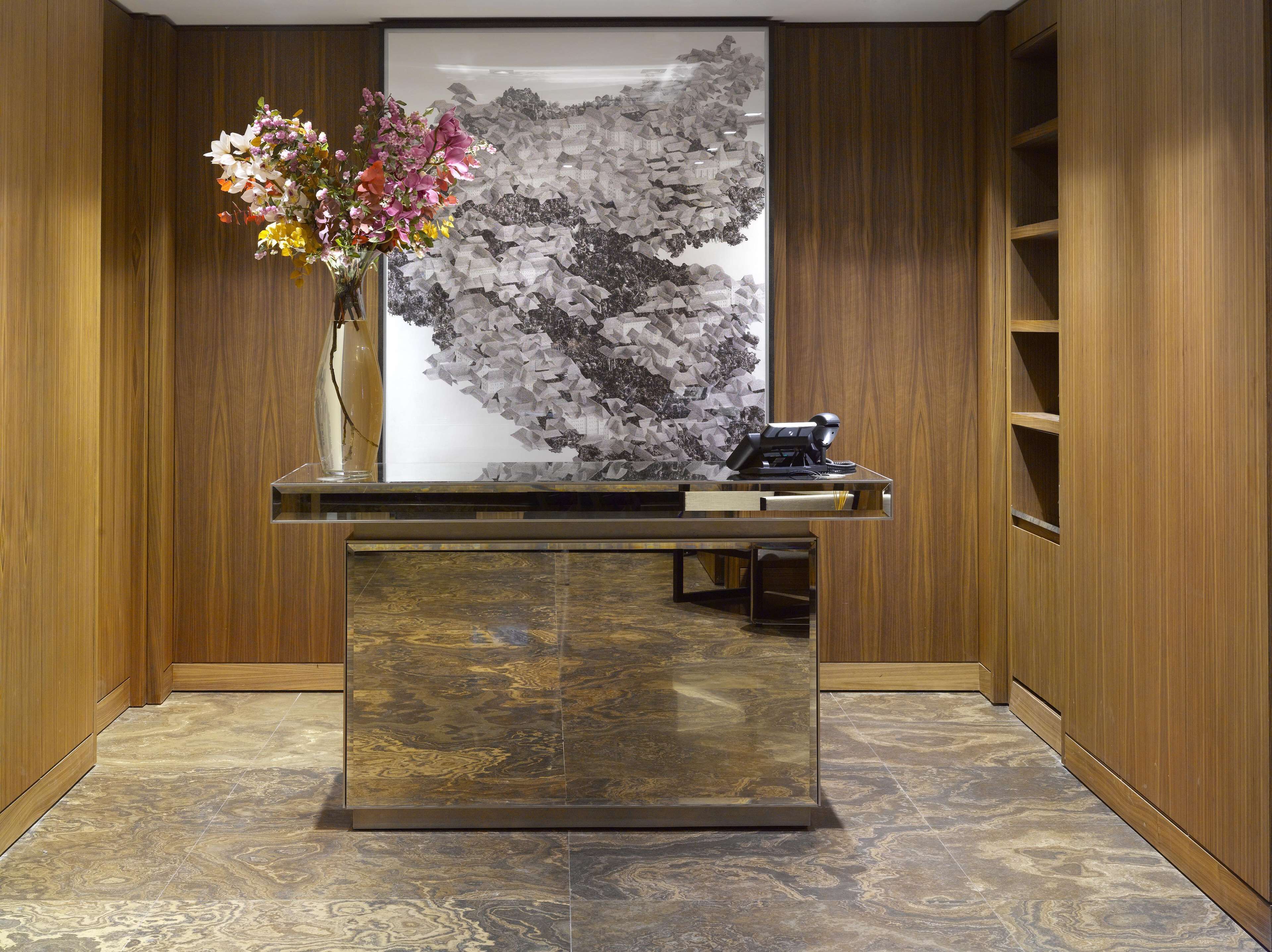 A reception desk with a vase of flowers, a black telephone, and a large framed artwork on the wall.