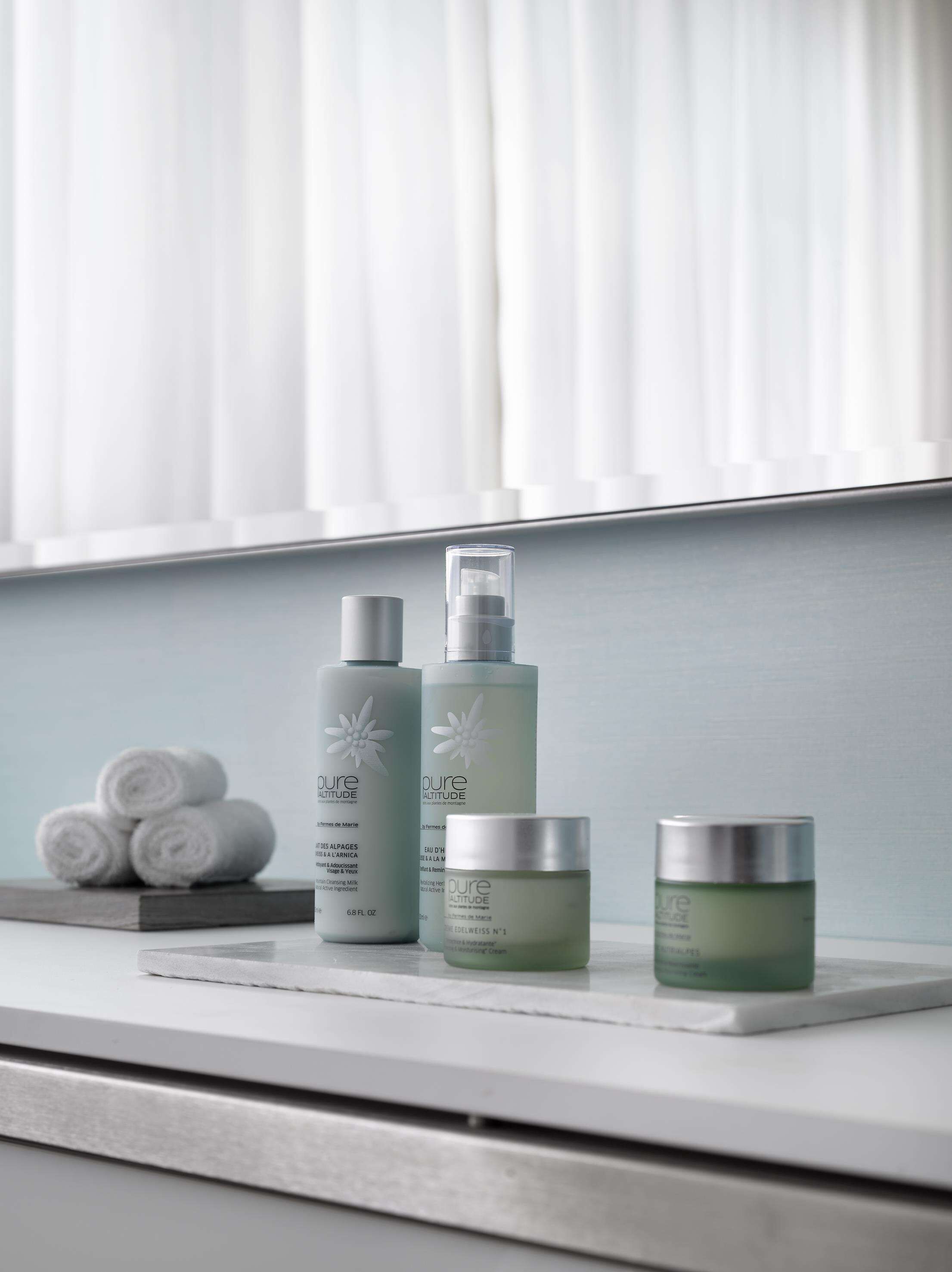Un meuble-lavabo de salle de bain avec un miroir, un porte-serviettes avec des serviettes et trois flacons de produits de soins pour la peau.